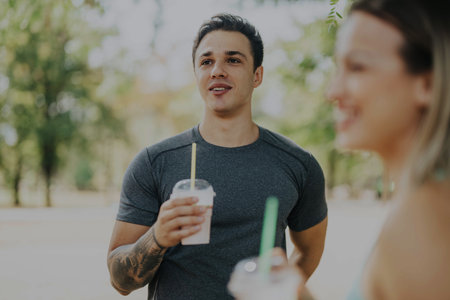 Friends enjoying refreshing drinks together in the sunny parkの写真素材