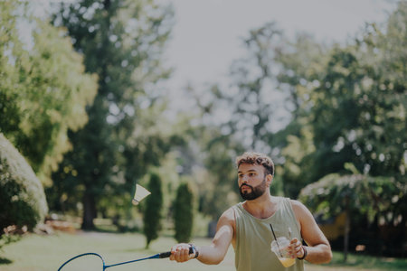 Young man playing badminton and enjoying a sunny day in the parkの写真素材