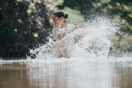 Woman joyfully playing in water creating refreshing splashes on a sunny dayの写真素材