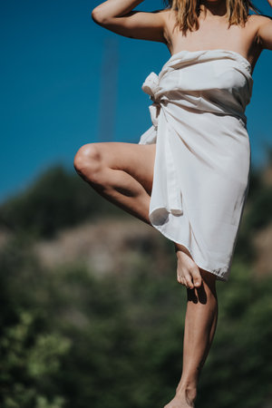 Woman in white dress posing outdoors in nature on a sunny dayの写真素材