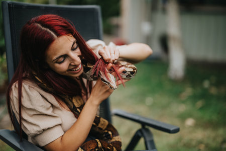 Girl with red hair smiling while holding a large snake outdoorsの写真素材