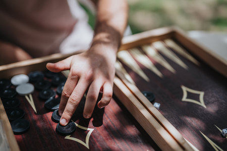 Hand playing backgammon game outdoors with sunlight creating a relaxing atmosphere on a wooden board