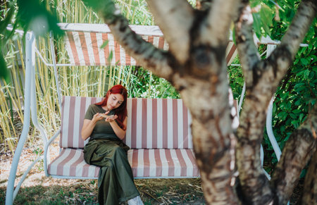 Young girl sitting on a garden swing, gently holding a lizard and enjoying natures tranquility in a lush green backyard setting.の写真素材