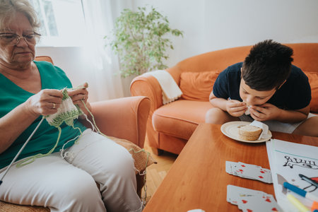 Grandmother knitting while her nephew enjoys a meal at homeの写真素材