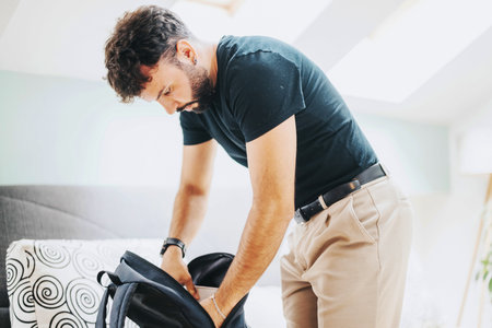Man packing backpack in sunny modern bedroom interior