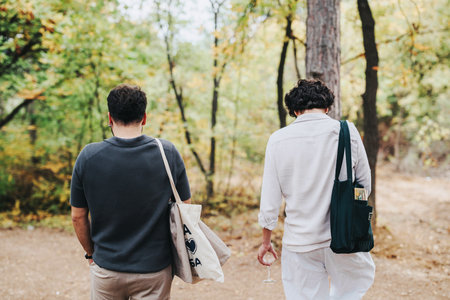 Two men walking through a serene forest carrying bagsの写真素材