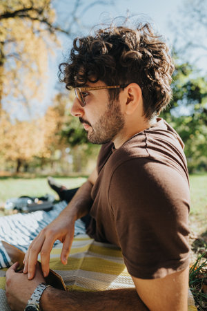 Young man relaxing outdoors on a sunny day, enjoying nature in a park setting, with a reflective and...