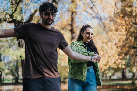 Young couple enjoying a playful walk through the autumn park with colorful leaves in the background....