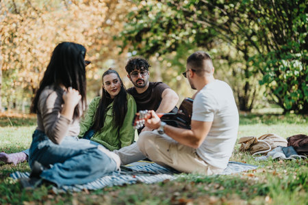 Group of friends enjoying a sunny autumn day in the park while playing music and sharing moments of...