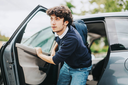 Teenage boy stepping out of car with backpack for schoolの写真素材