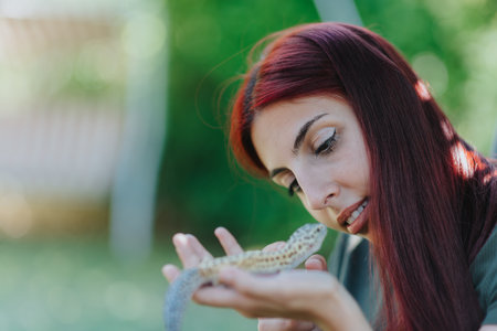 Young woman with red hair playing gently with a lizard in a garden setting exuding curiosity and fascination for wildlife and natureの写真素材