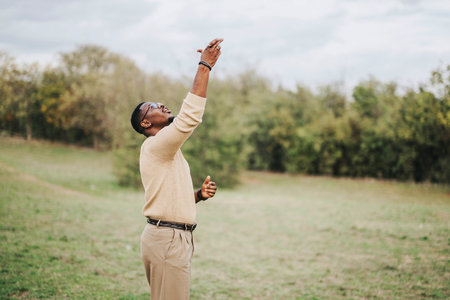A man stands in an open field with arms raised, embracing the tranquility of nature.の写真素材
