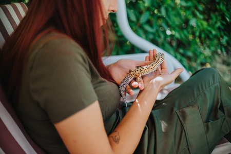 Girl gently playing with a spotted lizard outdoors on a chair, enjoying the natural setting.の写真素材