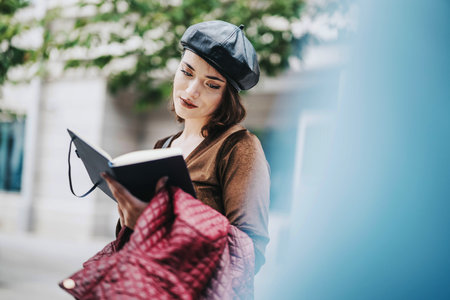 Young woman reading book outdoors wearing a stylish beretの写真素材