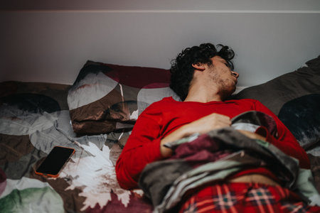 Young man peacefully sleeping in bed with smart phone nearbyの写真素材