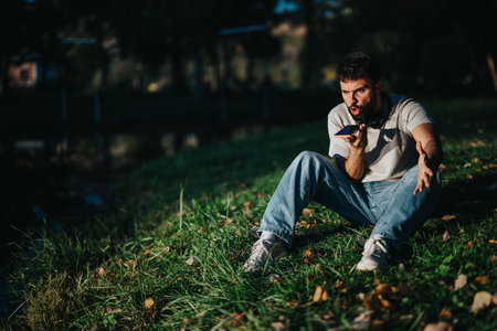Man sitting on grass using smartphone outdoors in a casual settingの写真素材