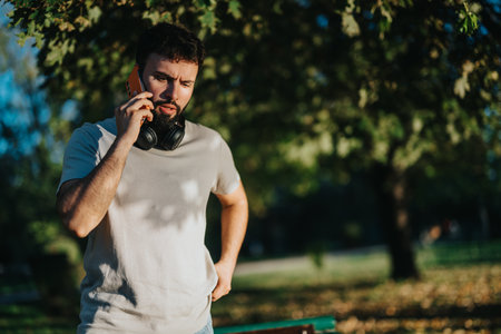 Young man talking on smart phone with headphones in a sunny park settingの写真素材