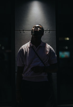 Moody street portrait captured under a single light source creating dramatic shadows in an urban environment at nightの写真素材
