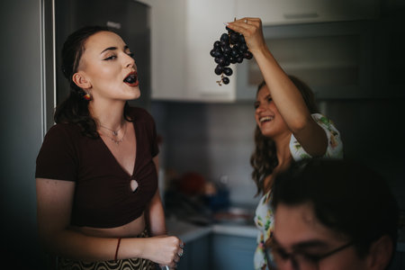 Two young women enjoying fresh grapes in a lively home setting, capturing joyful moments and friendship in a relaxed kitchen atmosphere.の写真素材