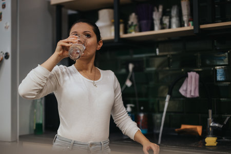 Woman enjoying a refreshing glass of water in modern kitchenの写真素材