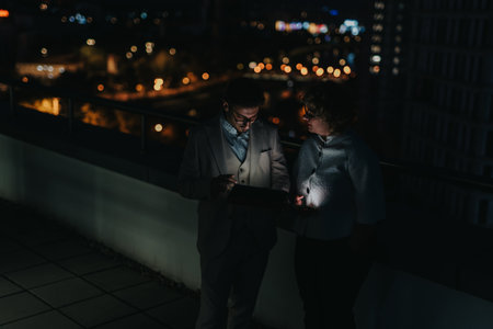 Two business people working on a rooftop at night analyzing dataの写真素材