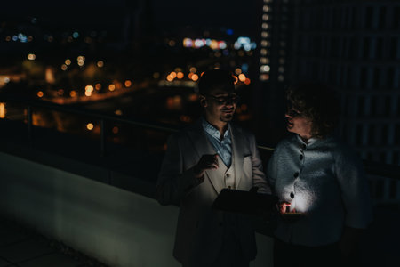 Business colleagues brainstorming on rooftop at night with city lightsの写真素材