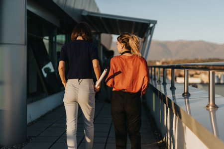 Two business colleagues walk on an office rooftop, engaging in a discussion about a project.の写真素材