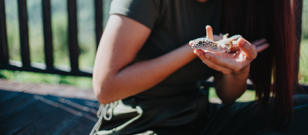 Young girl gently holding a lizard on her hands while sitting outside in a relaxed and natural environmentの写真素材