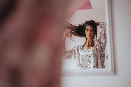 Woman styling long hair while looking into mirror reflectionの写真素材
