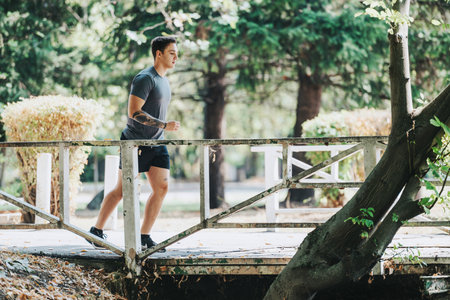 A man in athletic wear is jogging across a bridge in a lush green park.