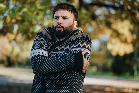 Man in cozy patterned sweater shivering outdoors in autumn seasonの写真素材