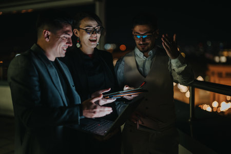 A team of business people collaborate outdoors at night using electronic devices.の写真素材