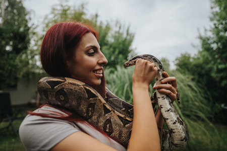 Young girl smiling while holding a snake outdoors in natureの写真素材