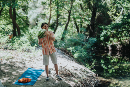 Young man enjoying nature by a peaceful river with a watermelonの写真素材