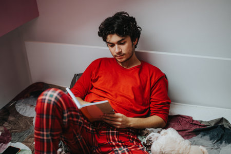 Young man reading a book while relaxing on his bedの写真素材