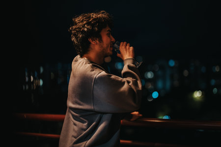 Man enjoying quiet evening drink on balcony with city lights