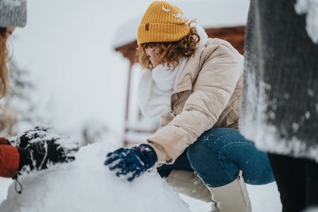 Woman Having Fun Building a Snowman with Friends in a Wintry Landscapeの写真素材