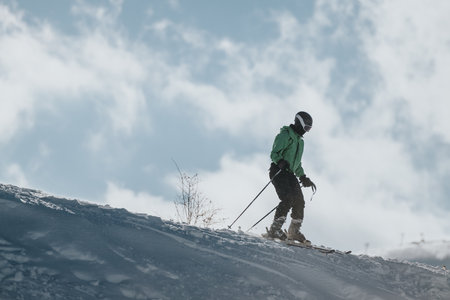Person in green jacket skiing on a snowy slope under a cloudy skyの写真素材