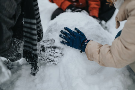 Group of individuals constructing a snowball together in a snowy outdoor setting