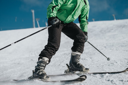 Person skiing on a snowy slope wearing green jacket with vivid backgroundの写真素材