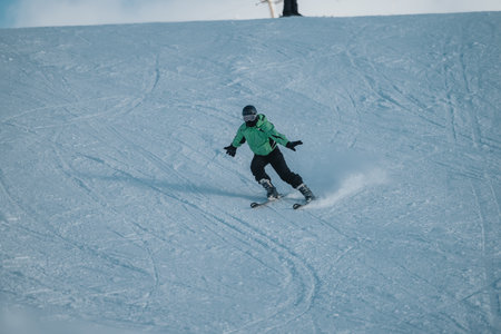 Person enjoying skiing down a snowy slope wearing green amidst a winter landscapeの写真素材
