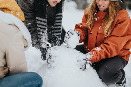 Group of friends building a snowman outdoors during winter, enjoying the snowy weather and fresh atmosphereの写真素材