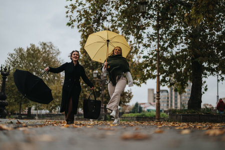 Two Smiling Women Walking with Umbrellas on a Rainy Day in Autumnの写真素材