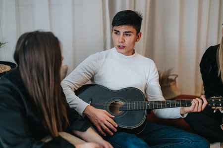 Young man playing guitar while talking to friends in a comfortable settingの写真素材