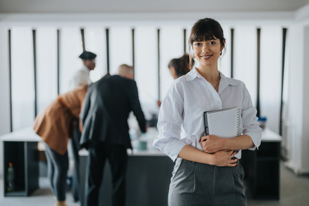 Confident professional holding notepad with colleagues collaborating in modern officeの写真素材