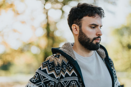 Thoughtful man outdoors wearing cozy knit sweater in autumn sunlightの写真素材