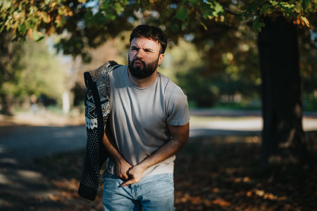 Man in casual attire squinting under bright sunlight in a park setting