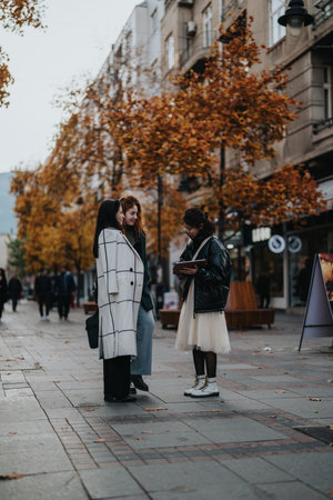 Three women conversing on an autumn street surrounded by urban sceneryの写真素材