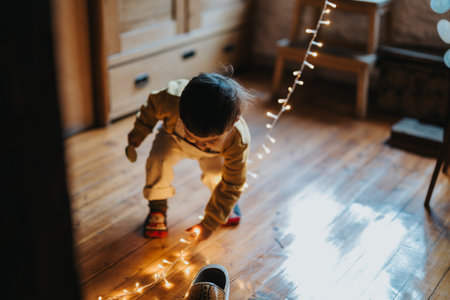 Young child playing with decorative string lights on a wooden floor in warm home settingの写真素材