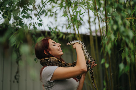 Girl joyfully holding snake in lush outdoor environmentの写真素材